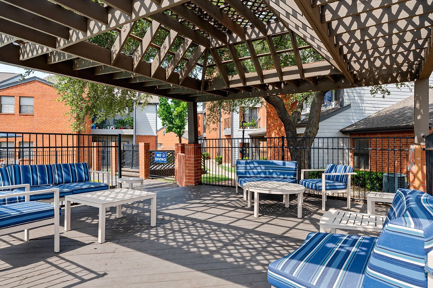 Outdoor seating area under a wooden pergola, with blue and white striped cushions.