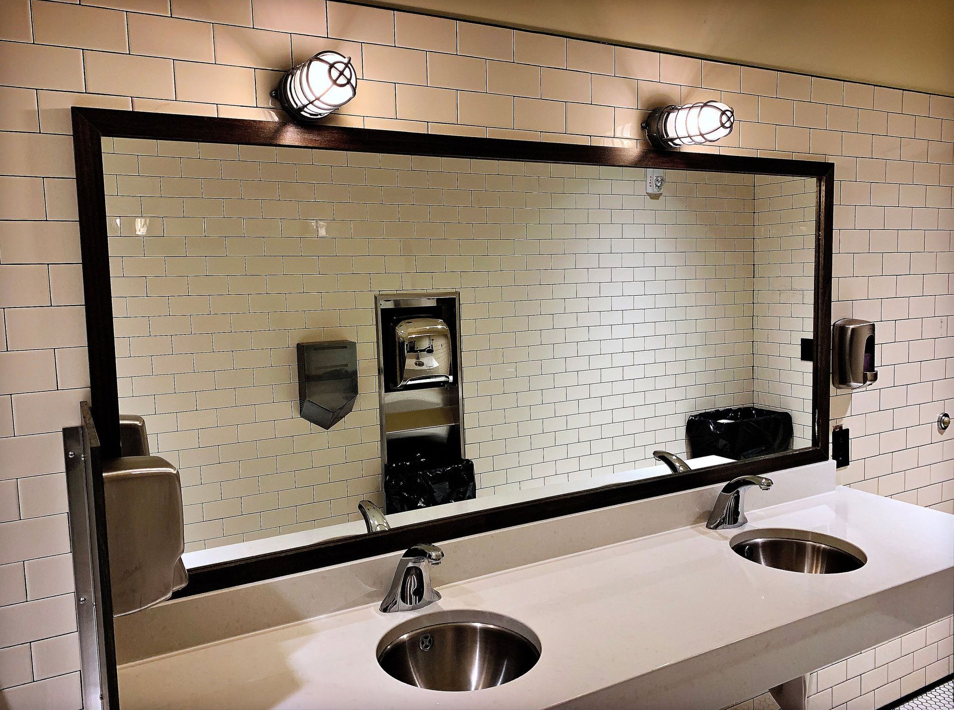 Public restroom with a large mirror, white sinks, and brick-like white tiles.