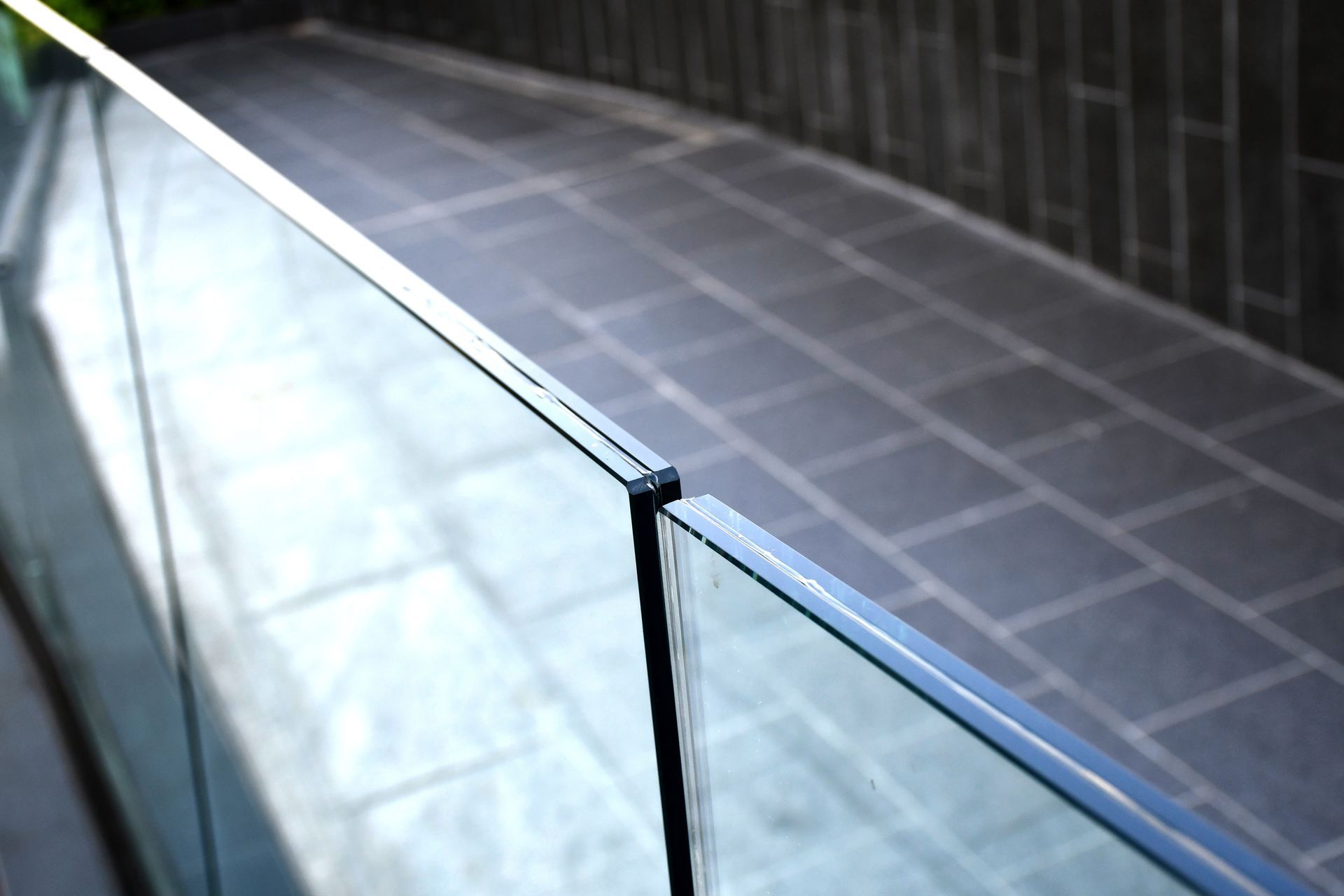 Glass railing, angled view, grey stone patio, dark brick wall in the background.