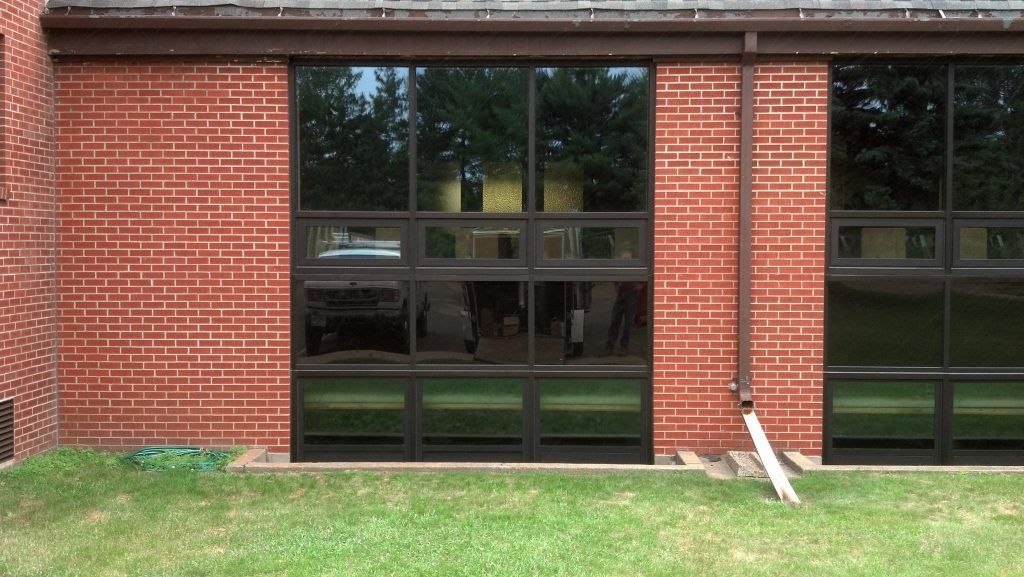 Brick building with large dark glass windows; green lawn in foreground.