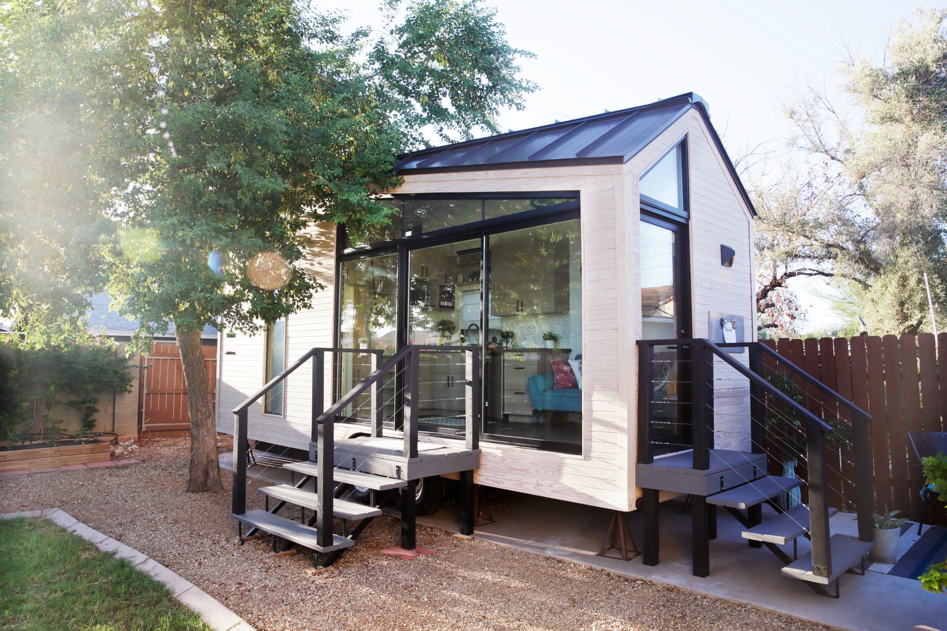 Tiny modern house with glass walls, steps, and metal roof in a yard.