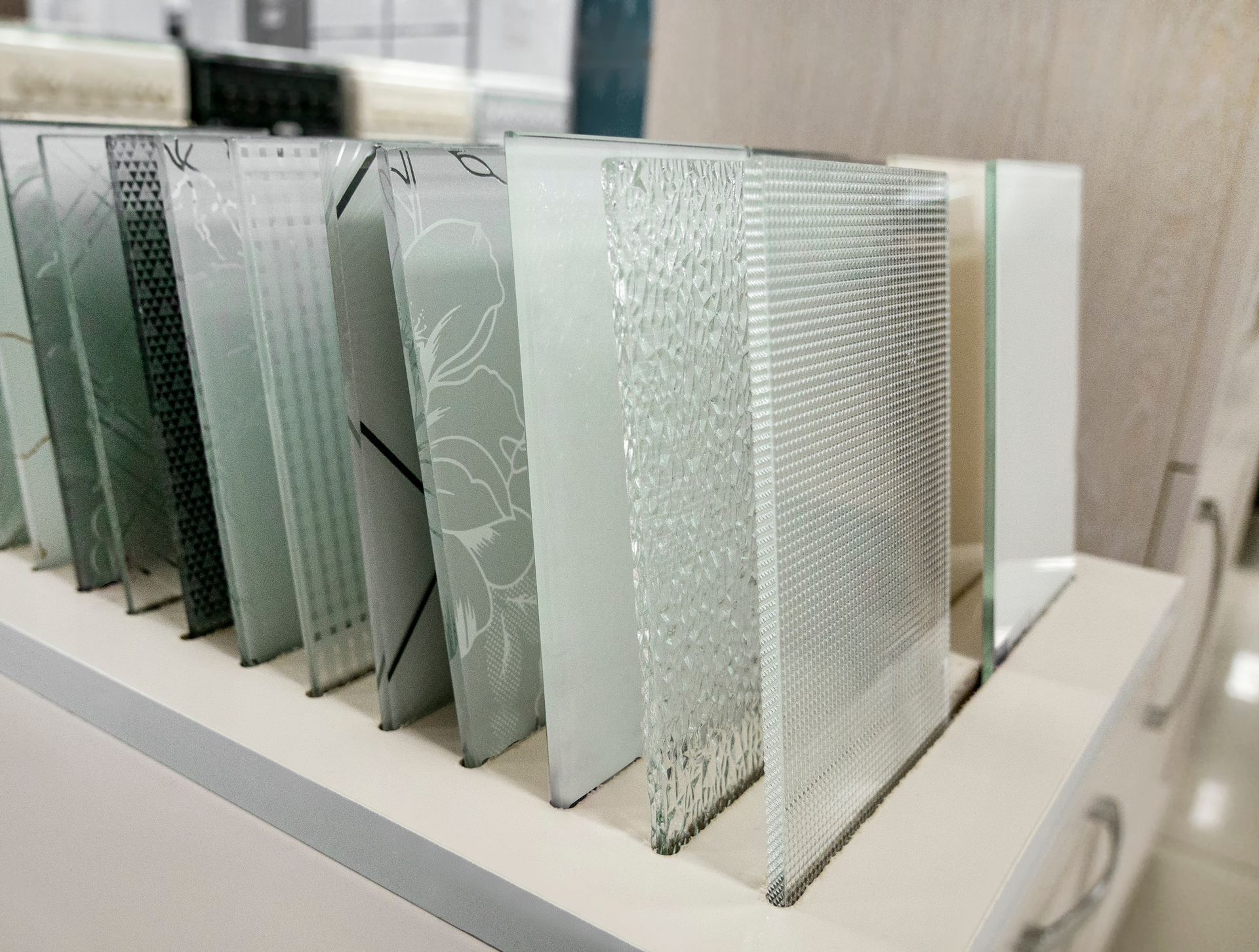 Display of various textured glass samples in a showroom, including clear, patterned, and frosted options.