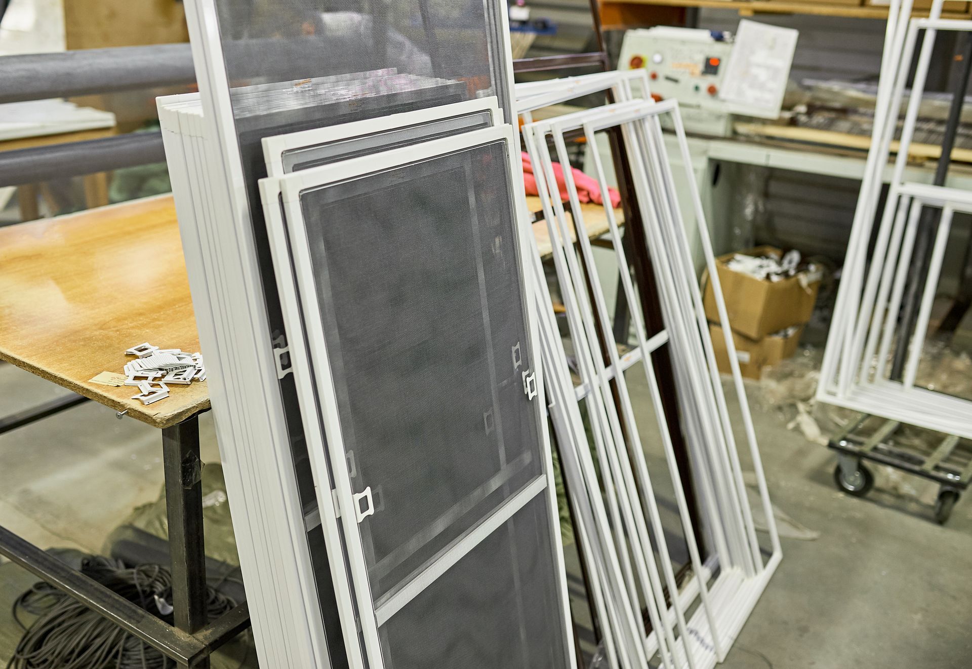 White-framed window screens stacked against a table in a workshop setting.
