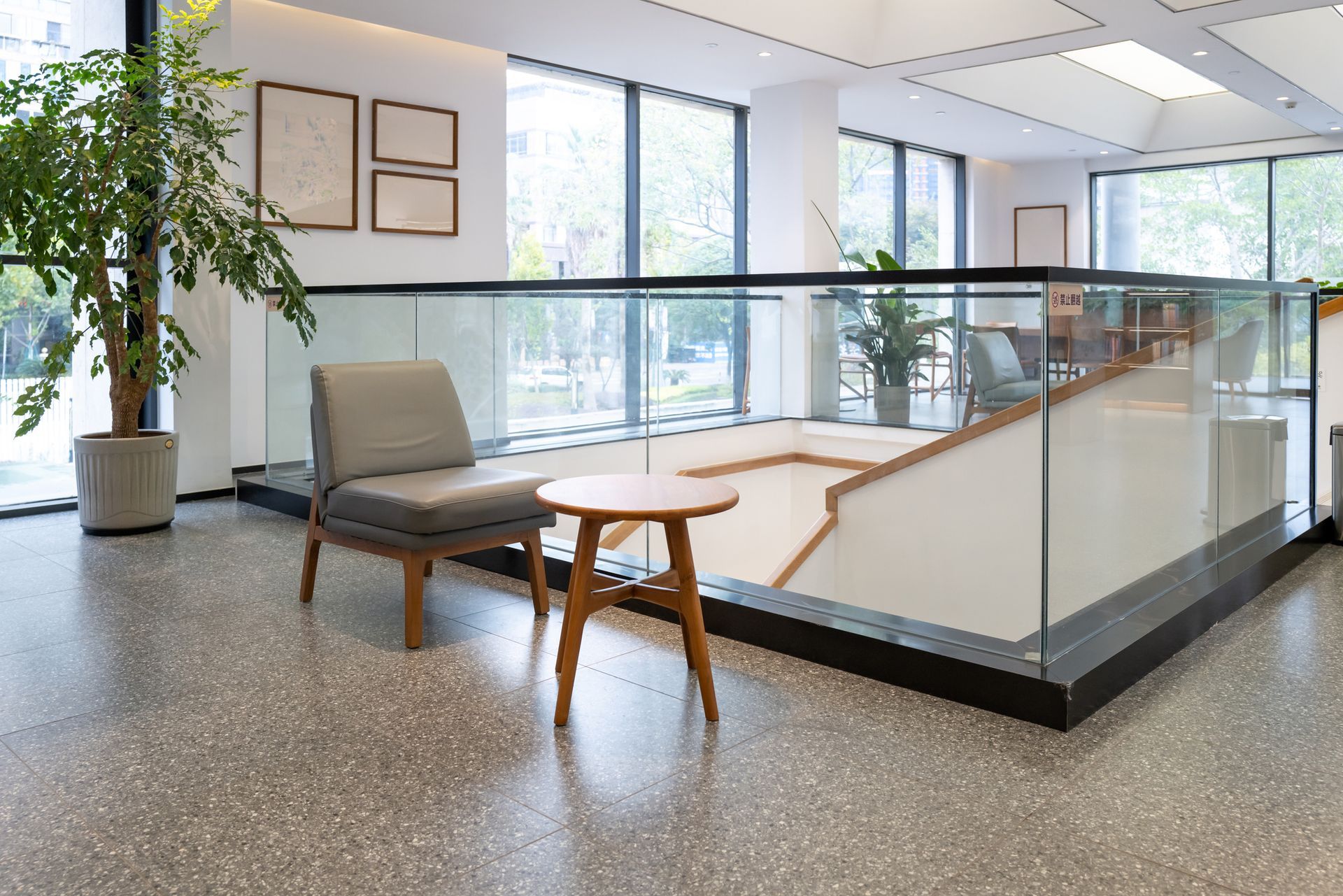 A modern waiting area with a chair, small table, and staircase behind glass railing.