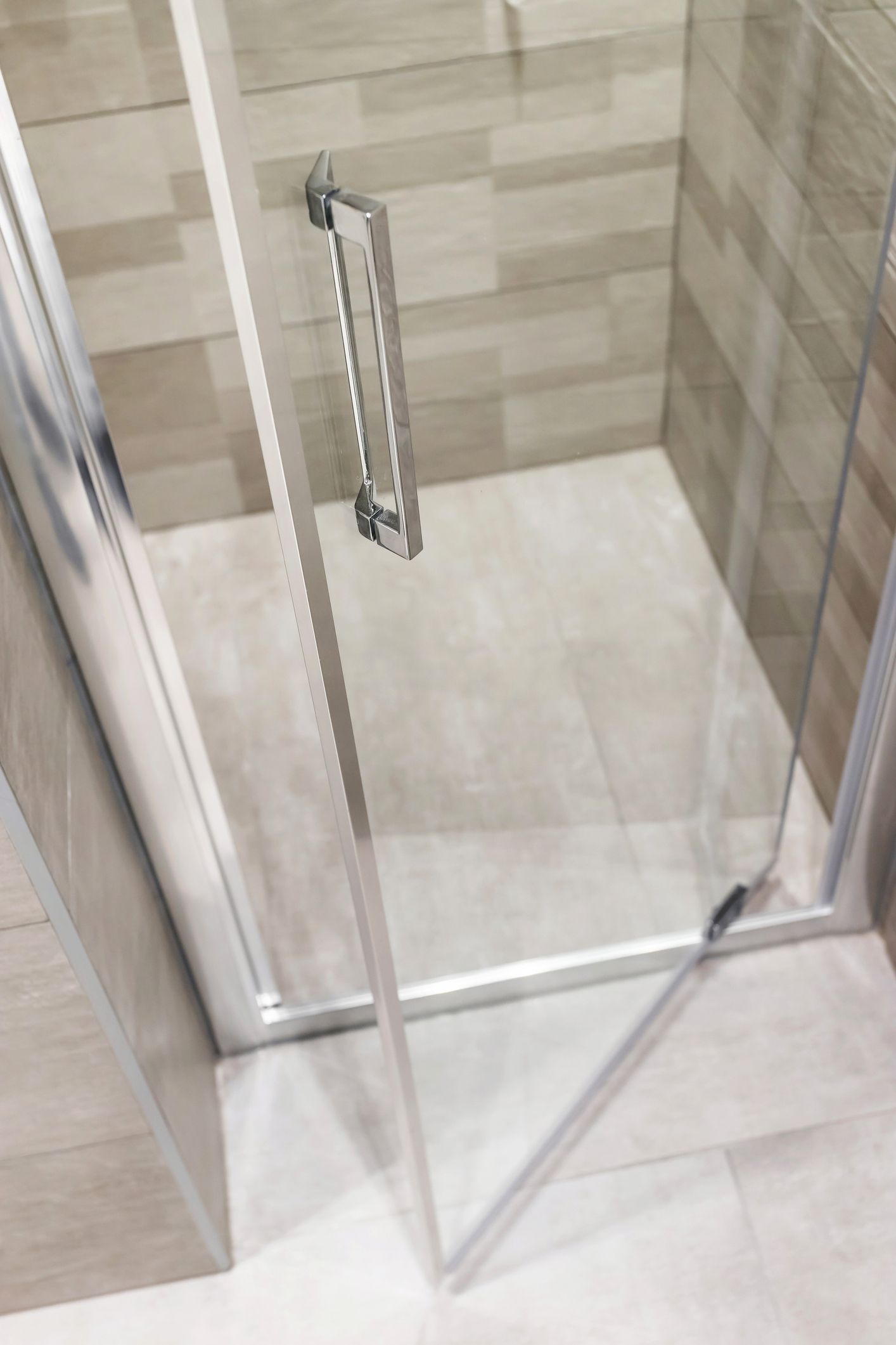 Glass shower door with silver handle, in a bathroom with light tile walls and floor.