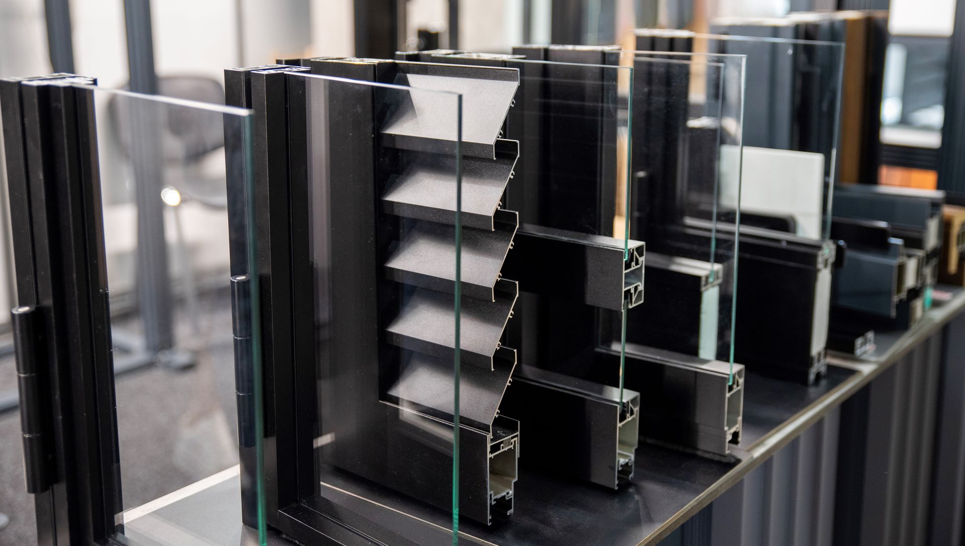 Black aluminum window frame samples displayed on a shelf.