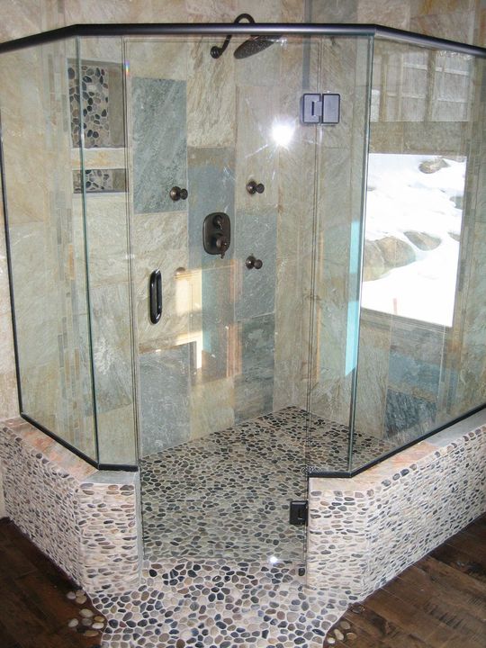 Corner shower with glass walls, pebble floor, stone tile, and black accents.