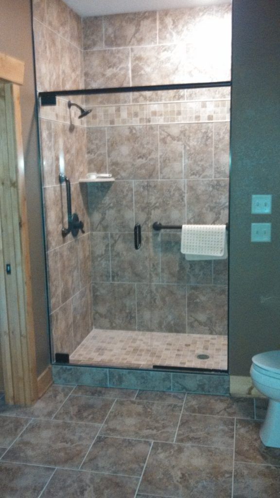 Shower with brown tile, black fixtures, and a glass door in a bathroom.