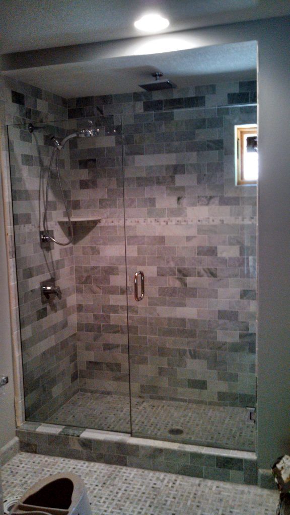Walk-in shower with gray brick-like tile, glass door, and silver shower fixtures.