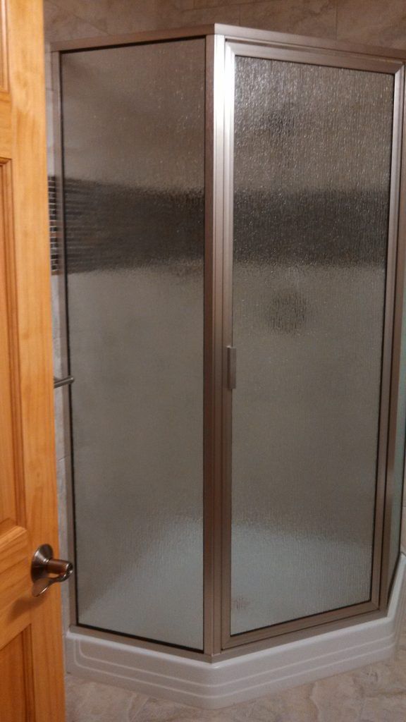 Glass shower enclosure with frosted panels and silver frame, adjacent to a wooden door.