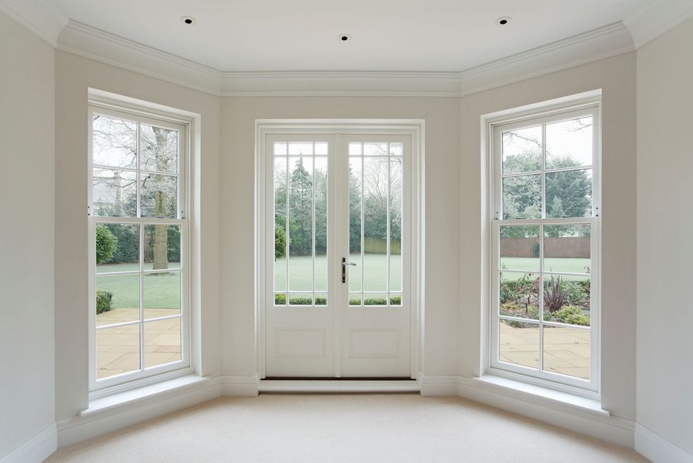 Bright, white room with three windows and double doors facing a garden.