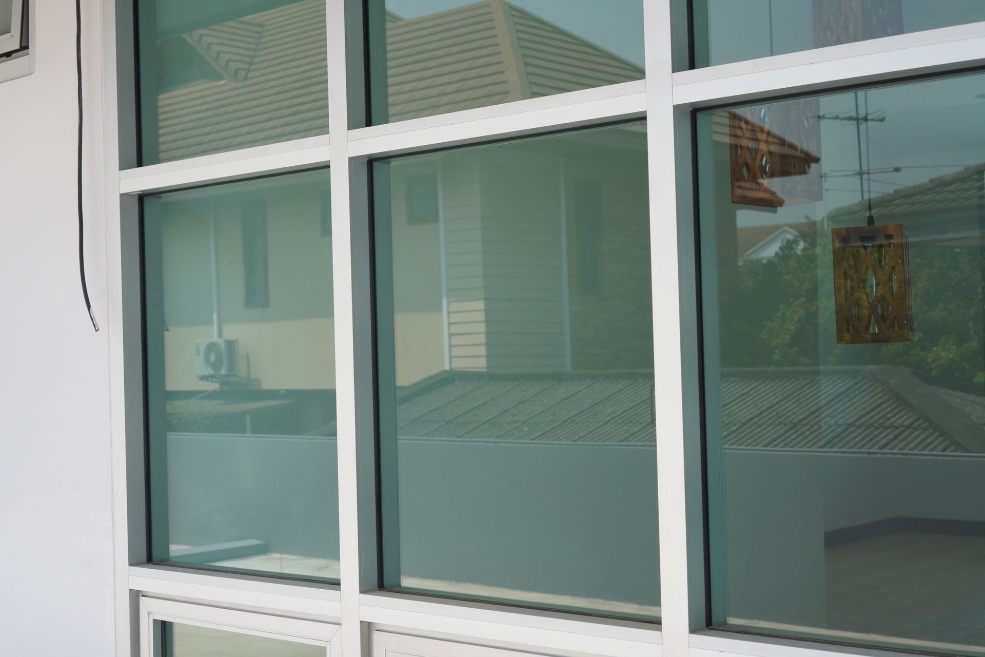 White-framed window with tinted glass, reflecting a building exterior, sky and antenna.