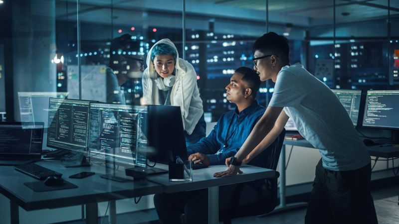 iverse team of IT developers collaborates late at night in a modern office, reviewing IT systems