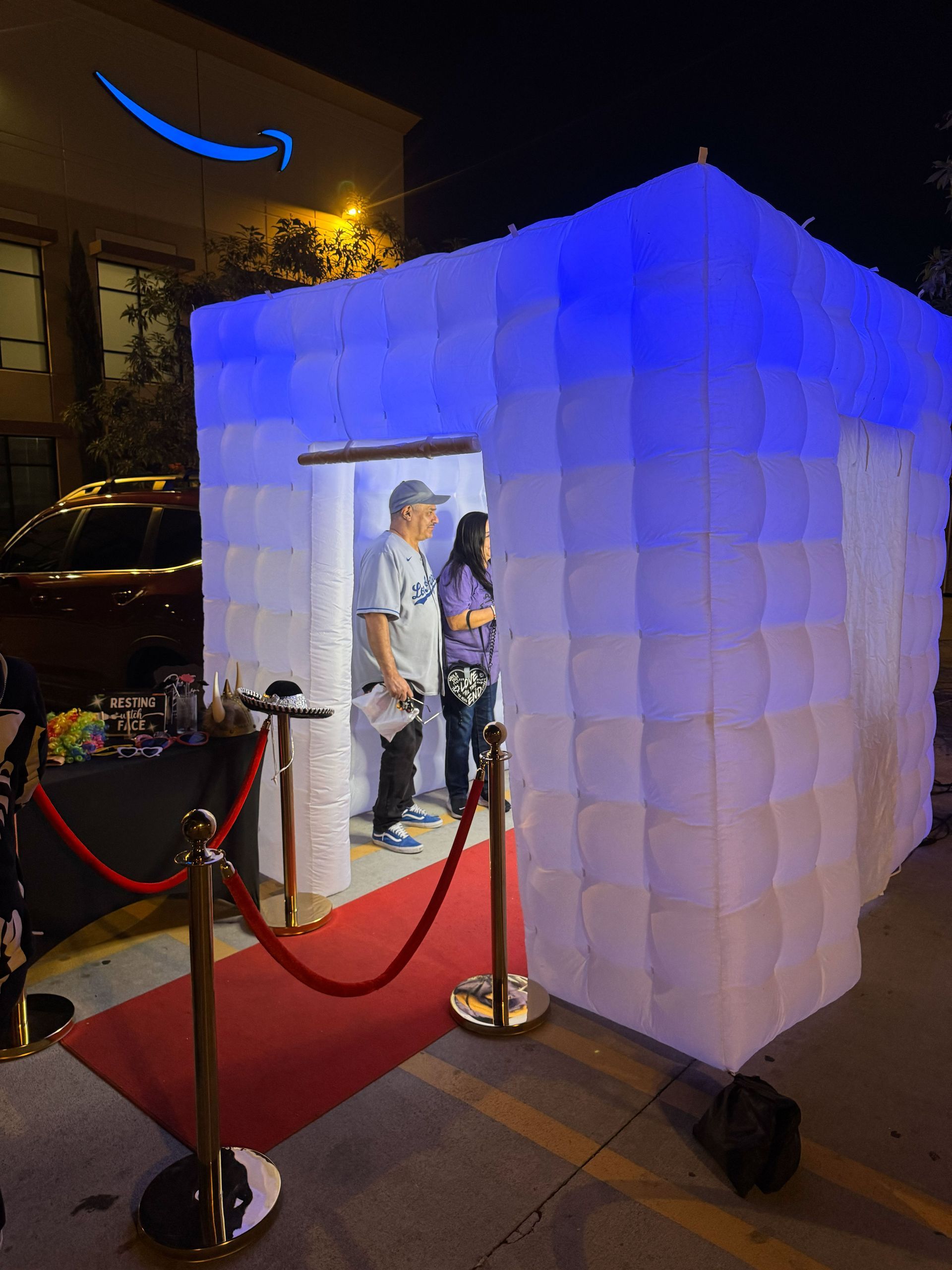 Couple embracing in front of a bokeh background. Man in hat and suspenders, woman in white dress, both smiling.