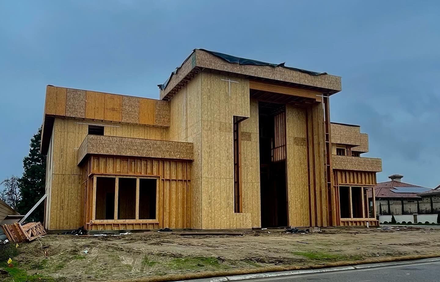 A large wooden house is being built on a dirt field.