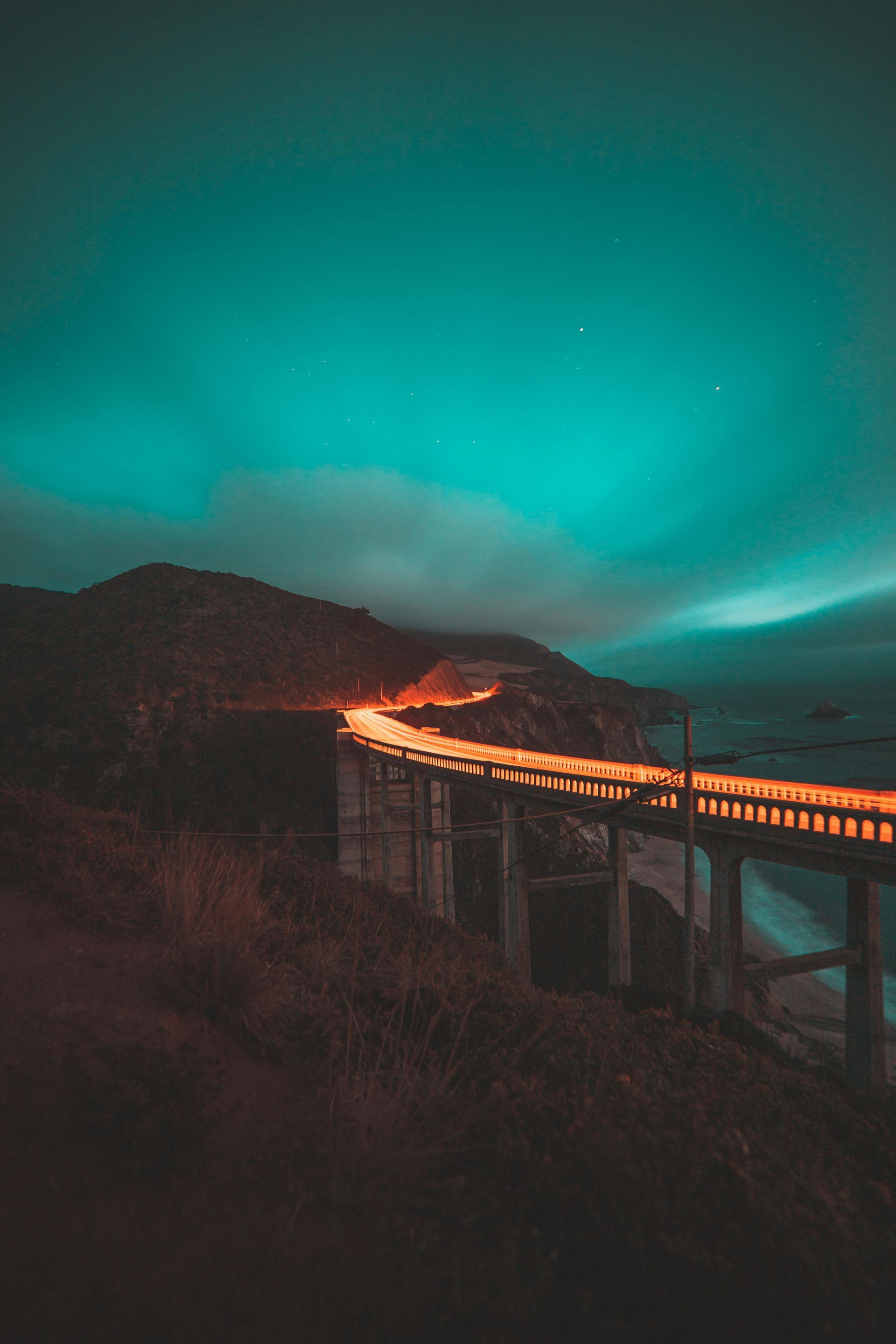 A bridge over a body of water at night with a blue sky in the background.