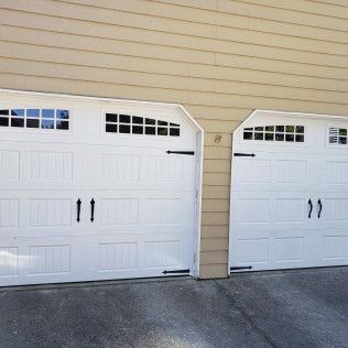 Two white garage doors with black hardware, under a beige building exterior.