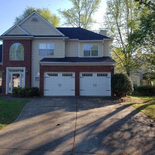 Two-story house with brick accents, two-car garage, beige siding, and a driveway on a sunny day.