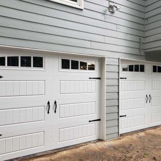 Two white garage doors with black hardware, set against a light blue-gray house exterior.