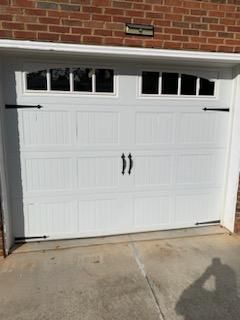 White garage door with black hardware, set in a brick building.