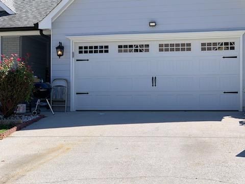 White garage door with decorative hardware, gray siding, and concrete driveway.