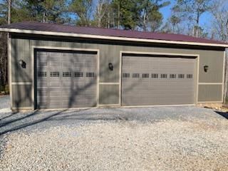 Two-car garage with grey doors, olive siding, and a gravel driveway.