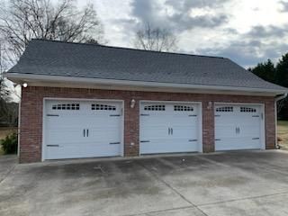 Brick three-car garage with white doors and dark roof against a cloudy sky.