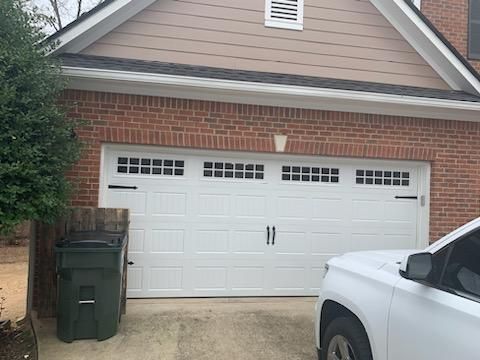 White garage door with black hardware, brick and tan siding, and trash can.