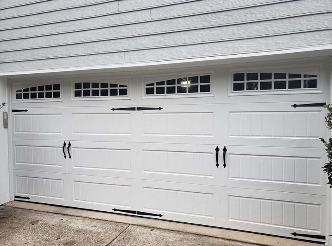 White garage door with decorative windows, black hardware, and white siding above.