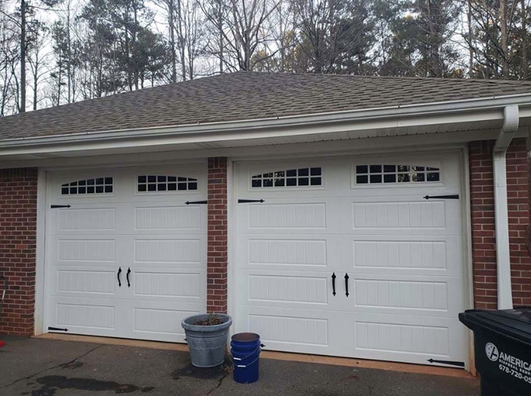 White garage doors with black handles and trim, brick facade, gray roof.