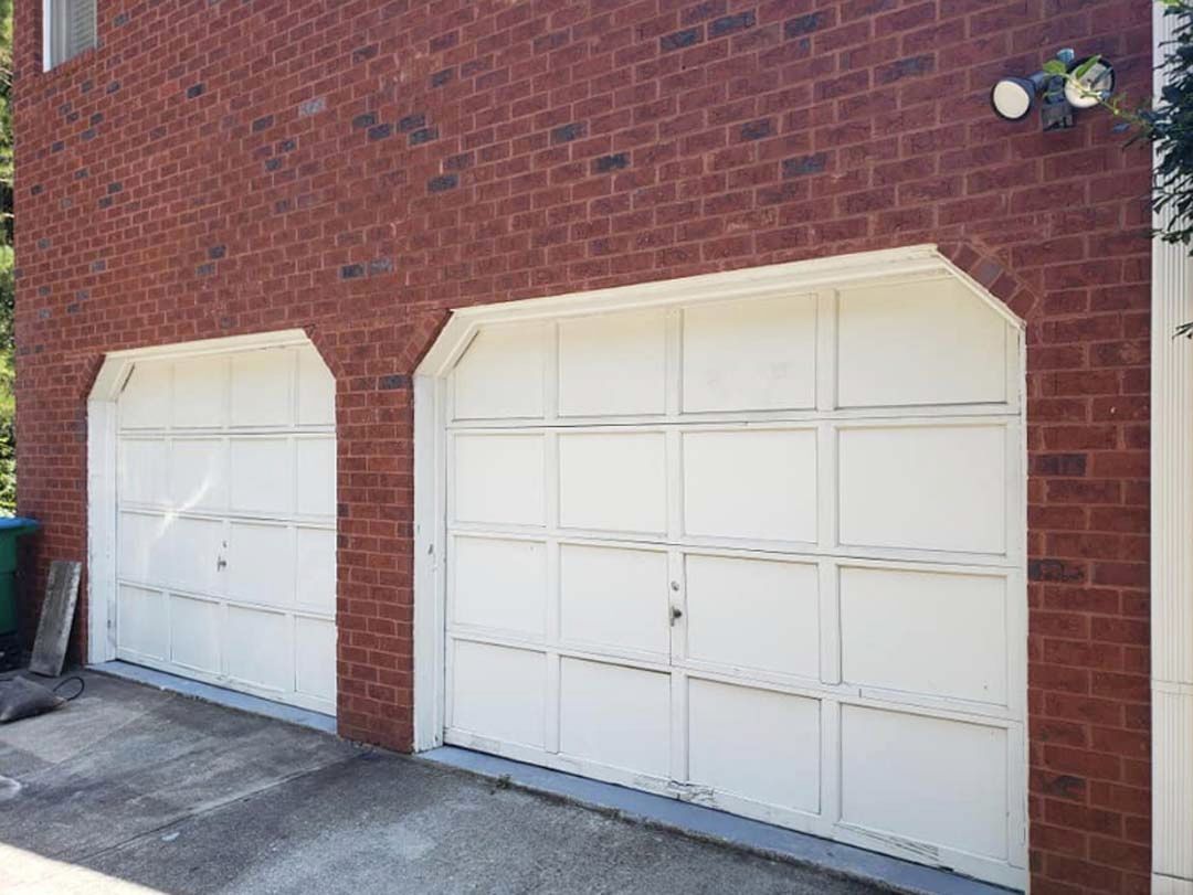 Two white garage doors with brick wall exterior.