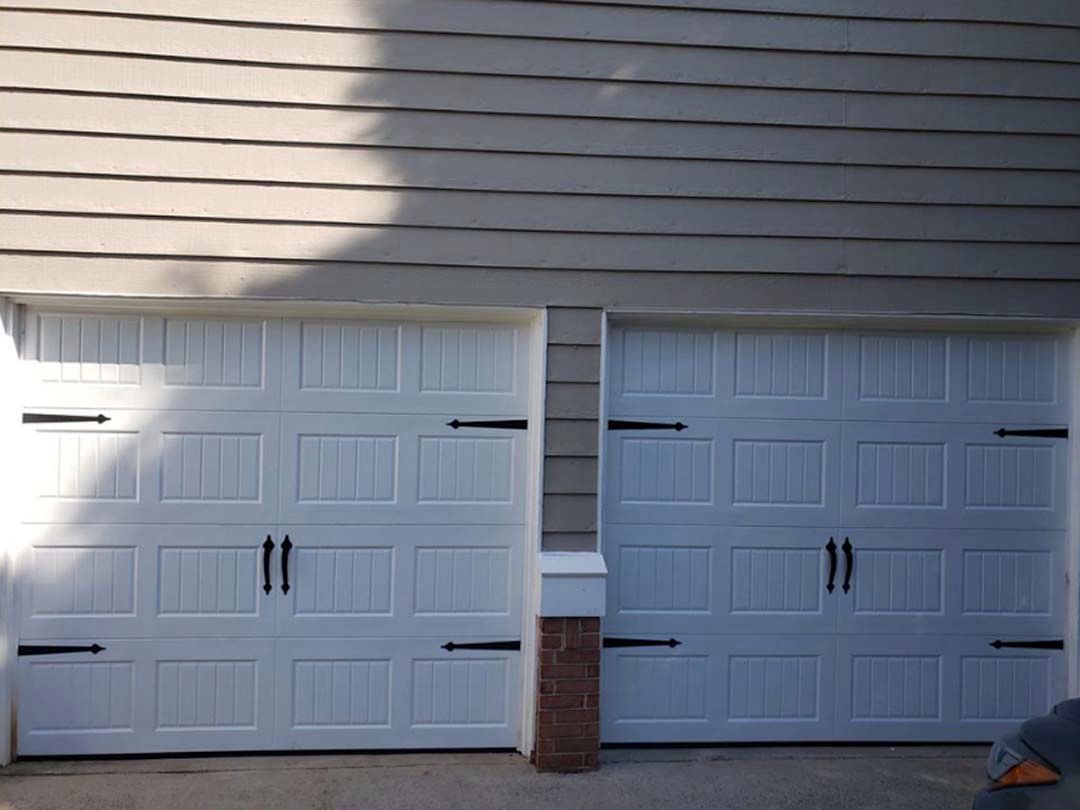 Two white garage doors with black hardware under a light-colored siding.