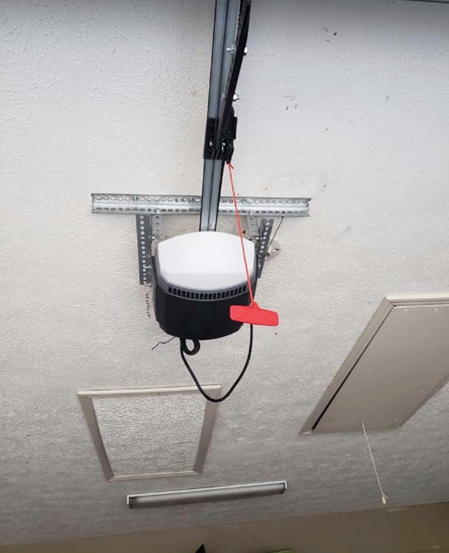 Garage door opener mounted on a textured white ceiling, with a red emergency release cord and two ceiling access panels.