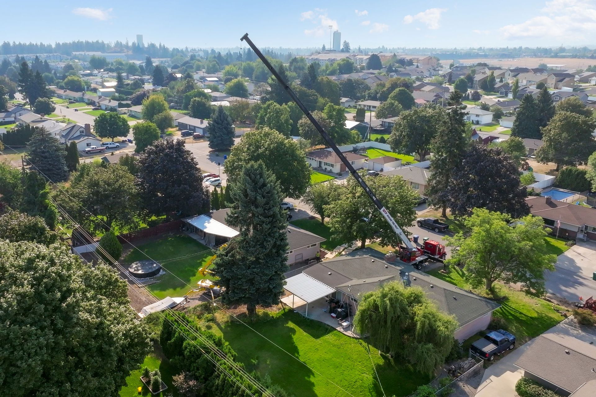 Crane working near residential houses with green yards and trees.