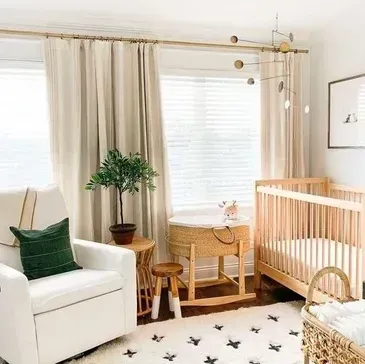 Cozy nursery with a crib, rocking chair, and neutral tones; a small tree and window coverings are also visible.