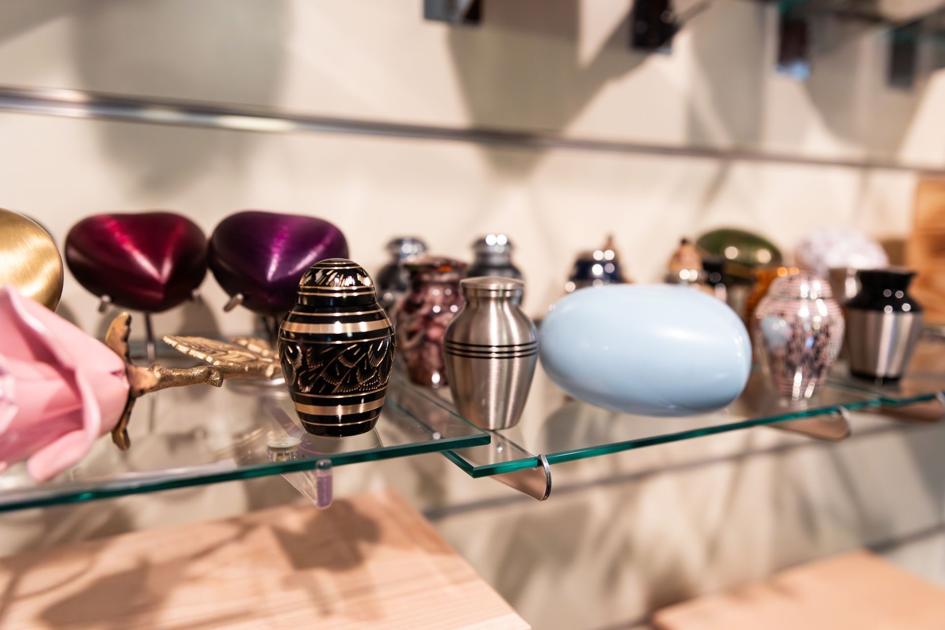 There are many different types of urns on display on a glass shelf.