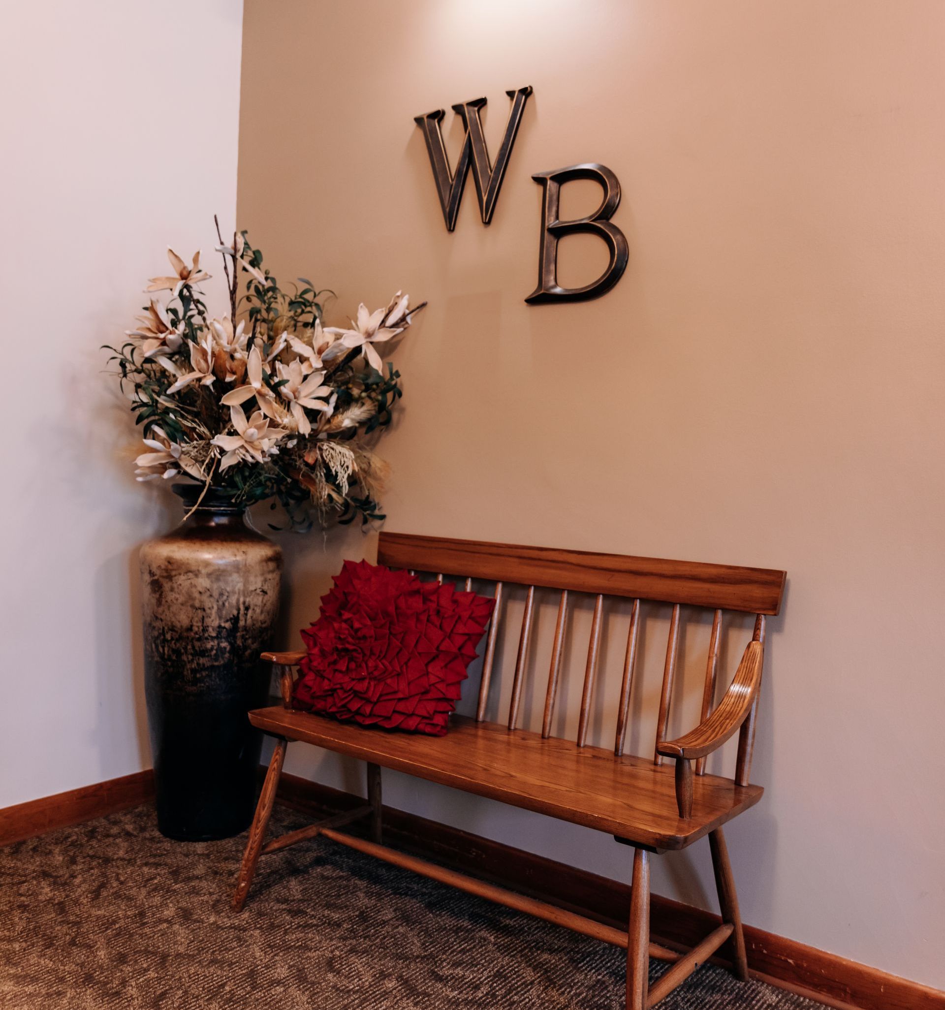 A wooden bench with a red pillow sits in front of a wall with the letter wb on it