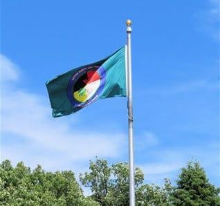 A green flag is flying in the wind on a pole.