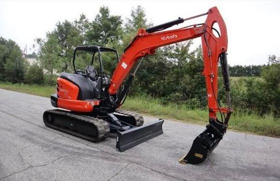 A small red excavator is parked on the side of a road.