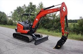 A small red excavator is parked on the side of a road.