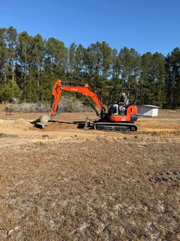 A large orange excavator is digging a hole in a field.
