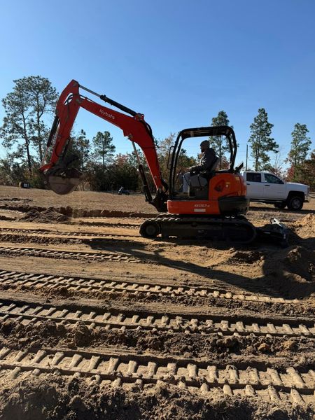 A man is driving an excavator on a dirt road.