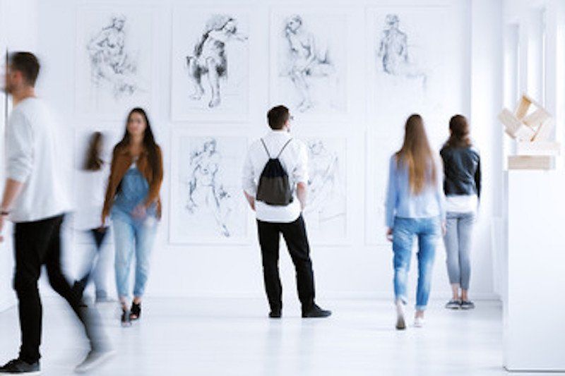 A group of people are looking at paintings in a museum.