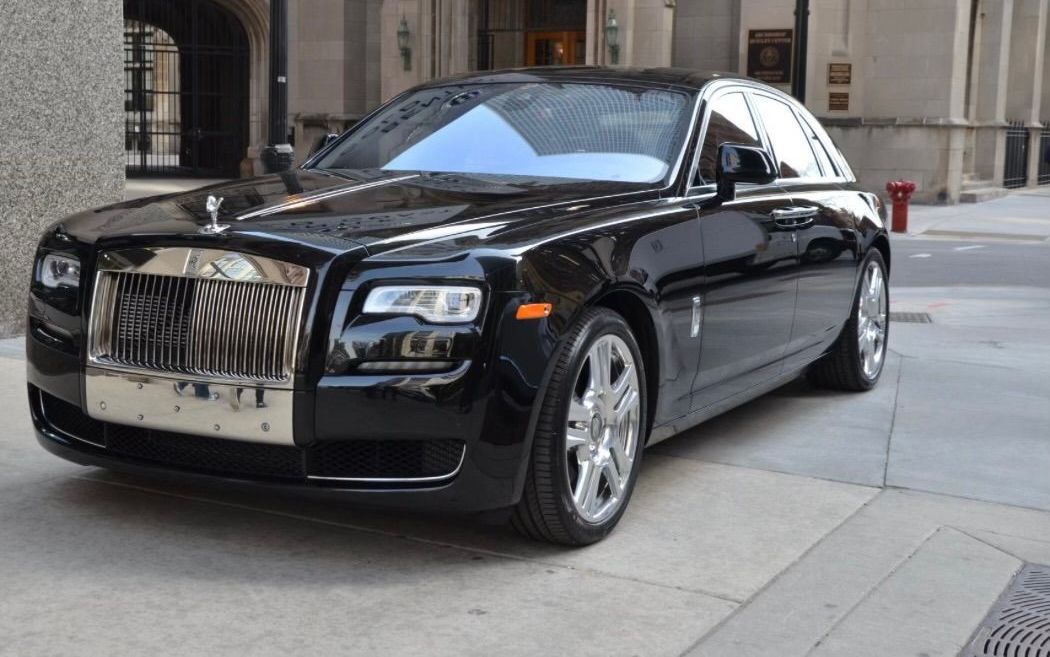 A black rolls royce is parked on the sidewalk in front of a building.