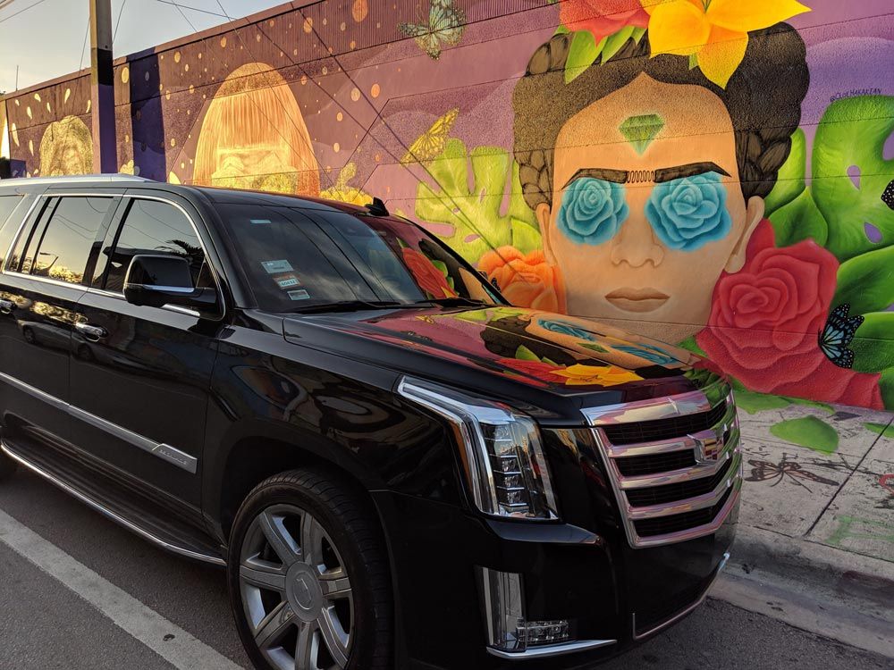 A black car is parked in front of a mural of frida kahlo.