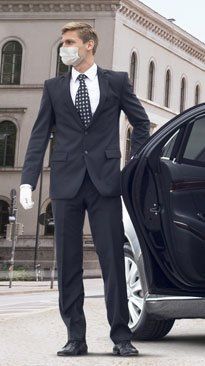 A man in a suit and tie wearing a mask is standing next to a car.
