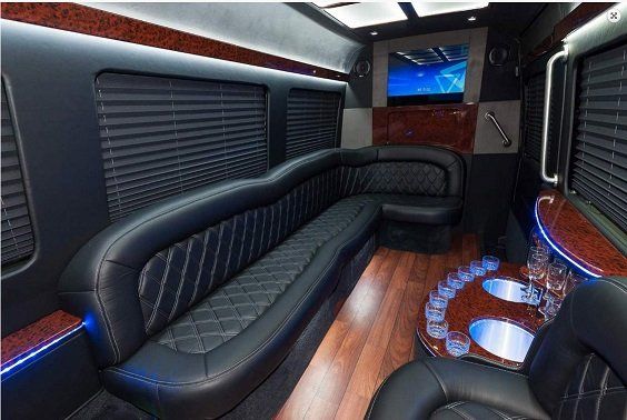 The inside of a limousine with a long black couch and a television.