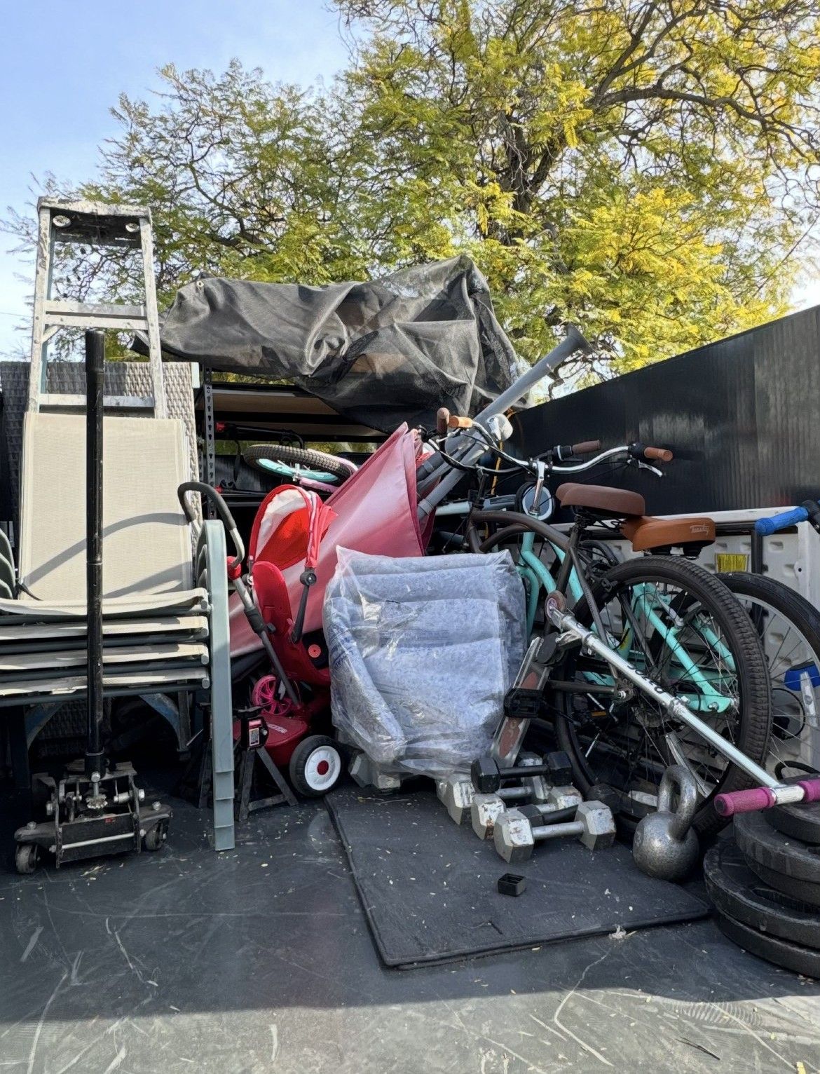 Truck bed filled with discarded items: bike, weights, ladder, red object, and other miscellaneous items.