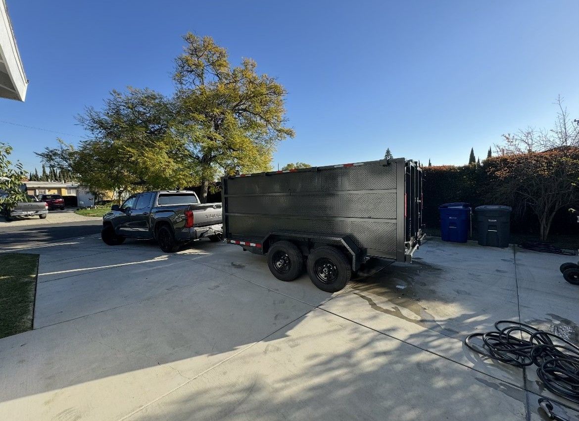 A truck pulling a large, black trailer in a driveway. Blue sky and trees in background.