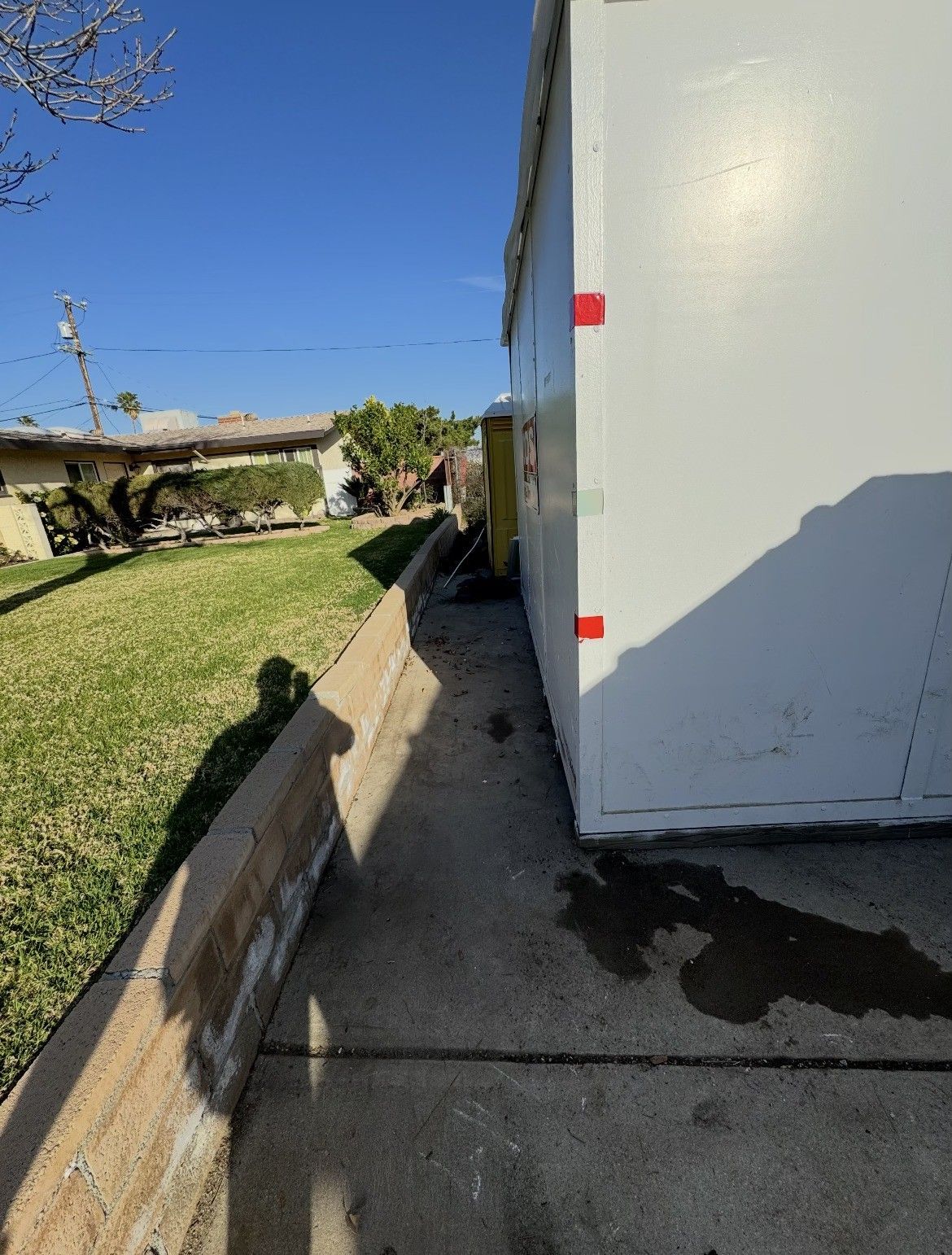 A narrow concrete path between a building and a retaining wall on a sunny day.